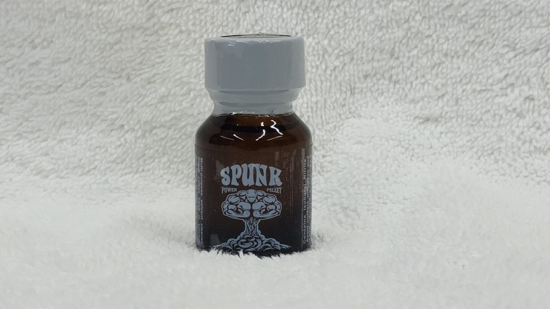 A small brown bottle of Spunk resting on a white textured surface.