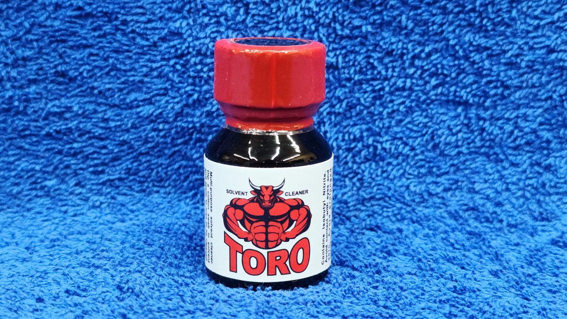 A small bottle of Toro solvent cleaner with a red cap, labeled with a graphic of a muscular lobster, on a blue textured background.