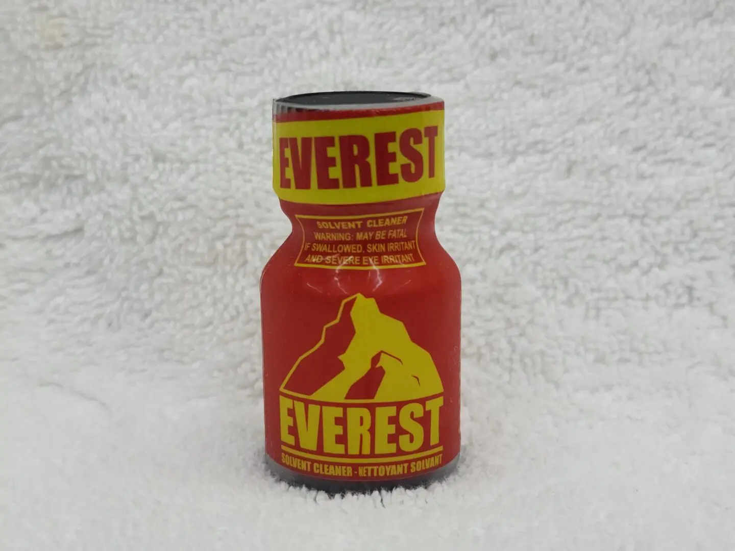 A red and yellow bottle of poppers sitting on top of a white blanket.