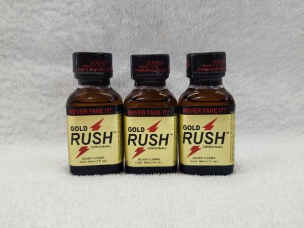 Three bottles of gold rush poppers on a white surface