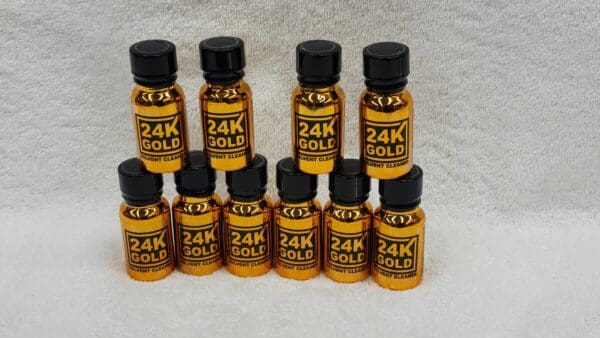 Nine bottles of 24K Gold arranged in three rows on a white fuzzy background.