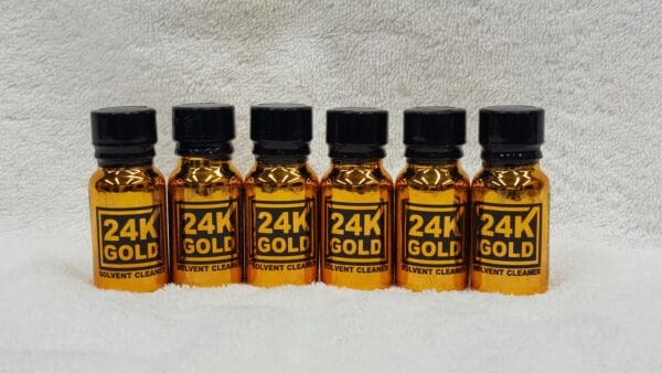 Five small bottles labeled "24K Gold" solvent cleaner lined up on a white towel.