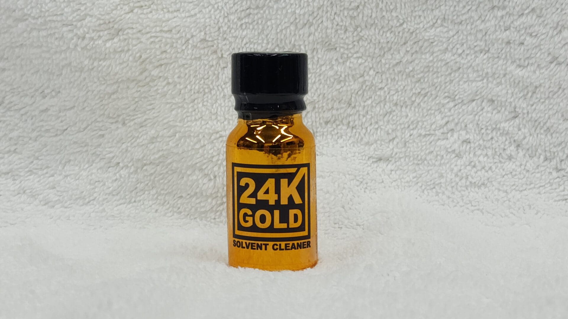 Sentence with product name: Small bottle labeled "24K Gold" on a white textured background.