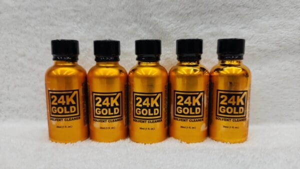 Four bottles of 24K Gold solvent cleaner aligned on a white surface.