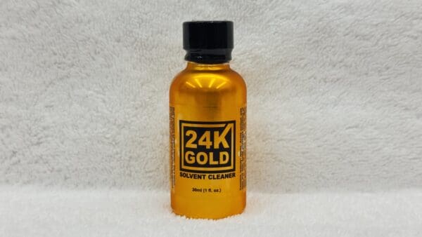 A small bottle of 24K Gold solvent cleaner on a white towel with clear branding on the label.