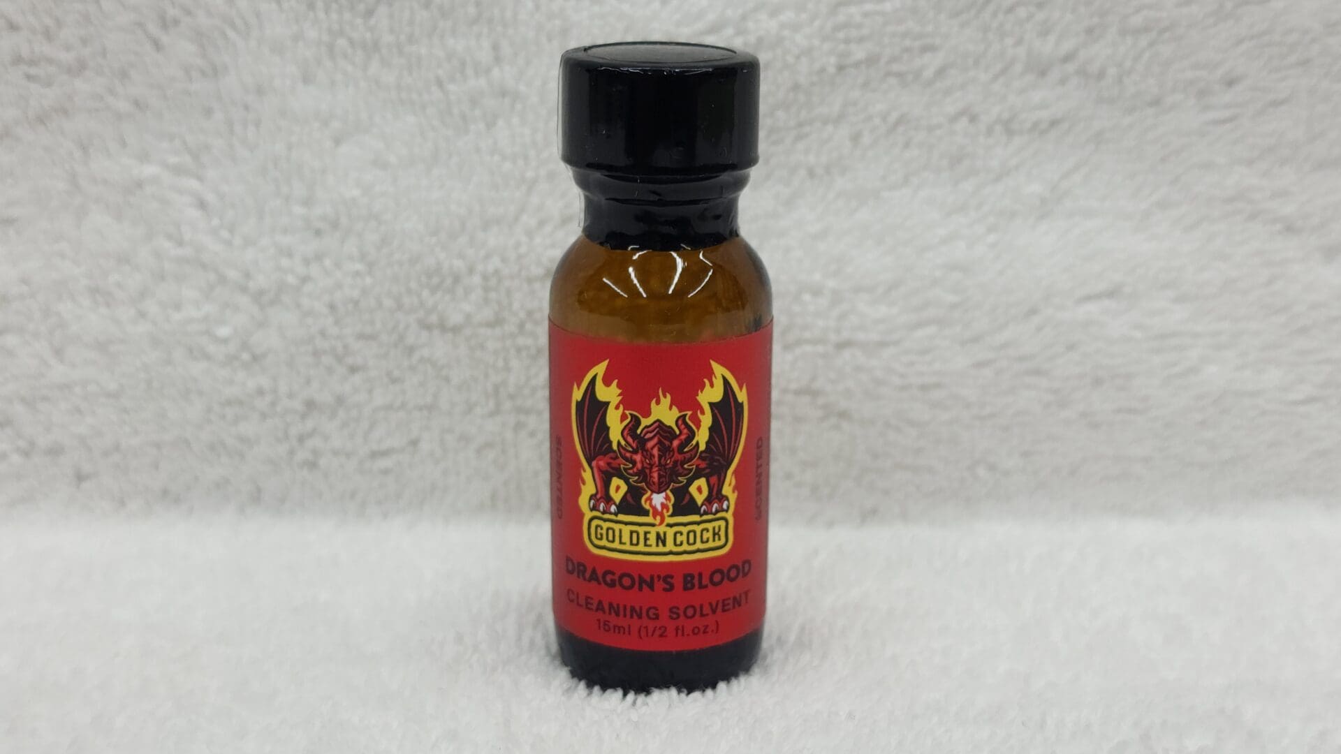 A small bottle labeled "Golden Cock Dragon's Blood" cleaning solvent on a white towel background.