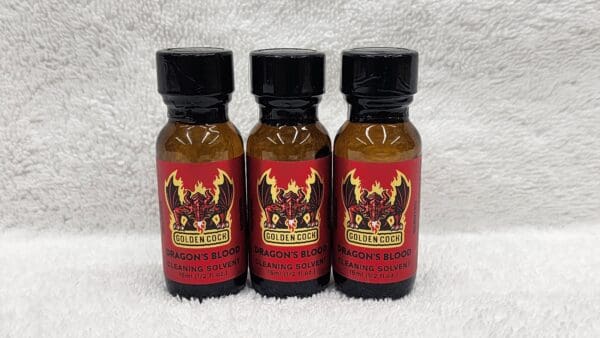 Three bottles of Golden Cock Original cleaning solvent on a white towel. Each bottle contains 1/2 fl oz of liquid.