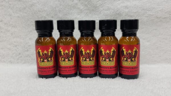 Five bottles of Golden Cock Original tanning bed lotion lined up on a white, fluffy surface.