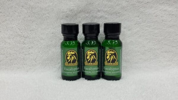 Three bottles of Golden Cock Original eucalyptus cleaning solution on a white textured background.