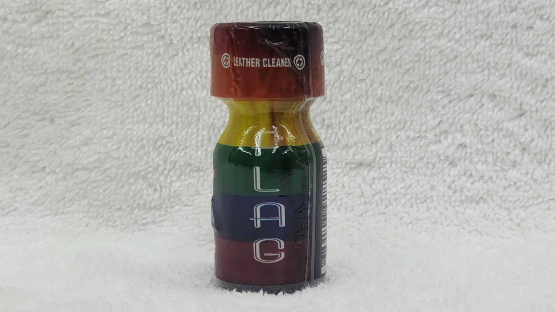 Small, multicolored glass bottle labeled "Jolt Flag" on a fuzzy white background.