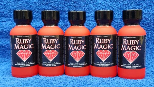 Five bottles of Ruby Magic solvent cleaner lined up on a blue towel, each bottle with distinct red color and labeled with a diamond icon.