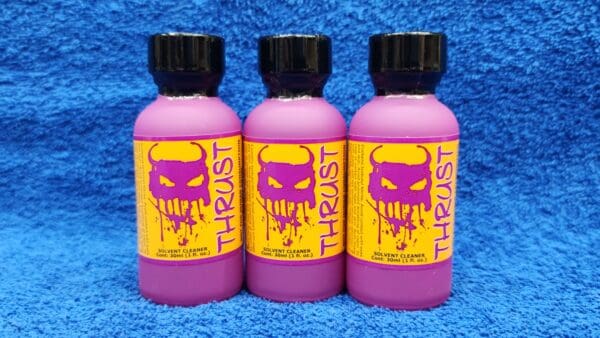 Three bottles of Ruby Magic solvent cleaner on a blue towel, each with a pink liquid and labeled in yellow and purple.