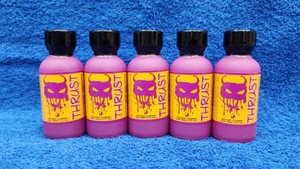 Five pink bottles of Ruby Magic brand lubricant with bright yellow labels, featuring a skull design, arranged in a row on a blue towel.