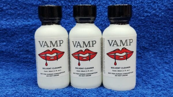 Three bottles of "Ruby Magic" solvent cleanser with red lips logo, aligned against a blue textured background.