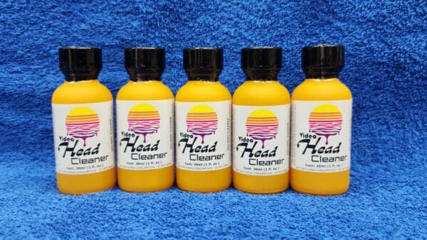 Five bottles of Video Head Cleaner on a blue towel, arranged in a row, with yellow liquid visible inside each bottle.
